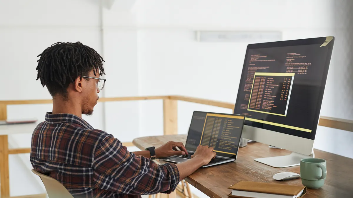 A Nigerian software developer reviewing AI-generated code on a dual-screen setup in a modern tech office